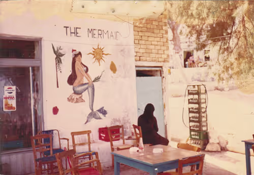 mermaid cafe A historic view of the Mermaid Café in Matala, Crete, with its hand-painted mermaid mural, outdoor tables and chairs, and rustic seaside setting.