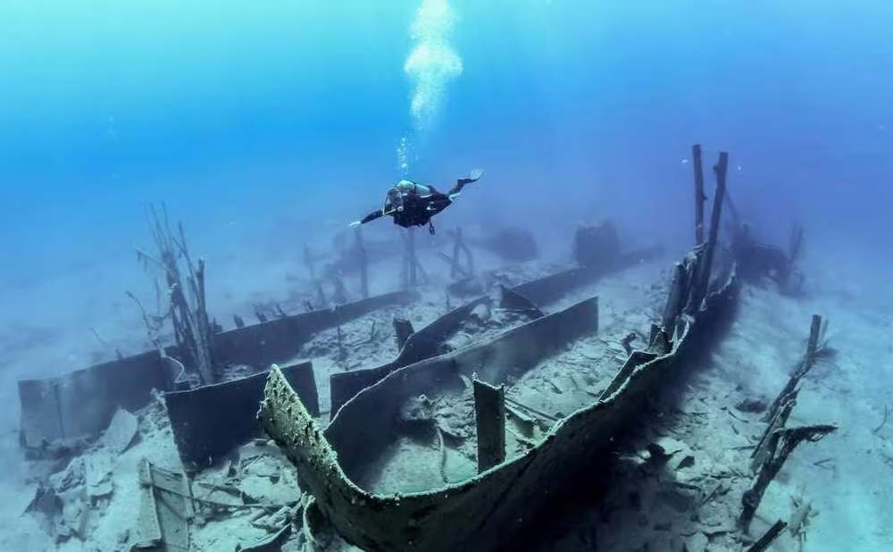 certified_diver_crete (1) A certified scuba diver exploring a sunken wooden shipwreck in the clear blue waters off Crete.